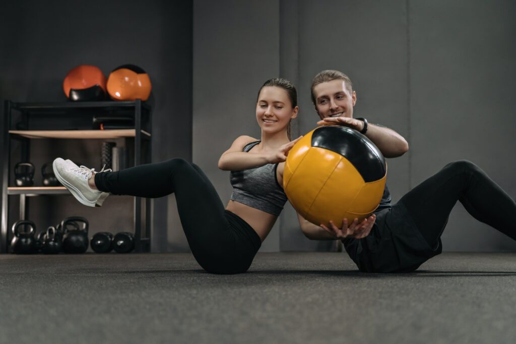 Happy fitness couple doing exercise with medicine ball at gym